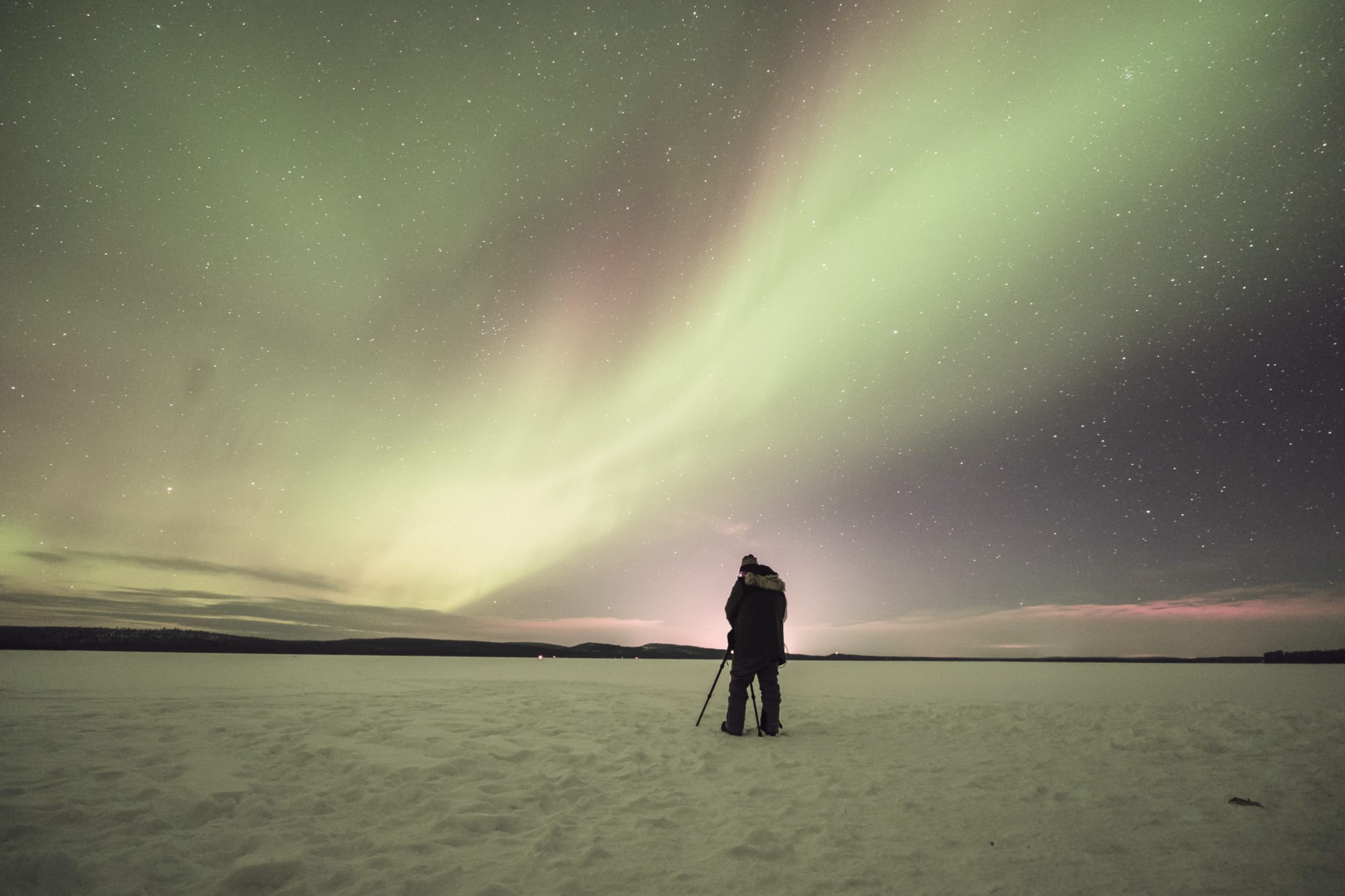 A photographer with a tripod on a frozen lake under the aurora